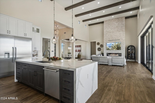 kitchen featuring appliances with stainless steel finishes, an island with sink, sink, white cabinets, and hanging light fixtures