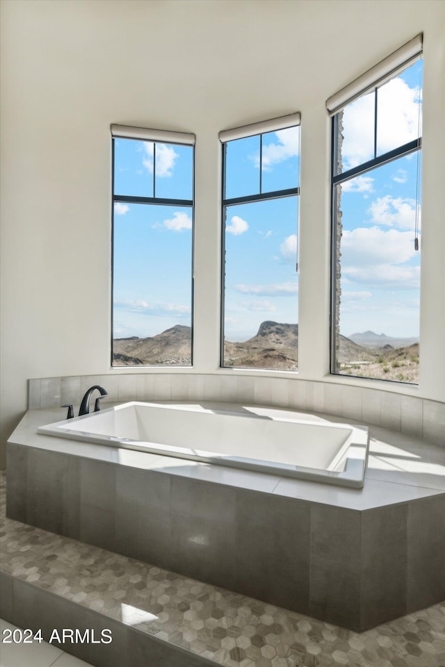 bathroom featuring a mountain view, a wealth of natural light, and tiled bath