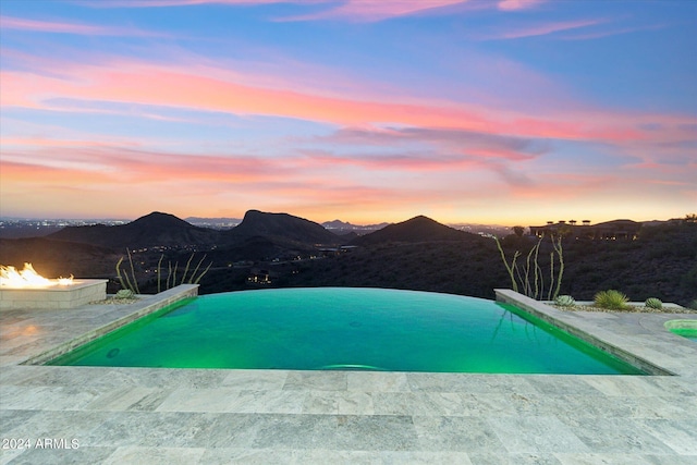 pool at dusk with a mountain view, a patio area, and an outdoor fire pit