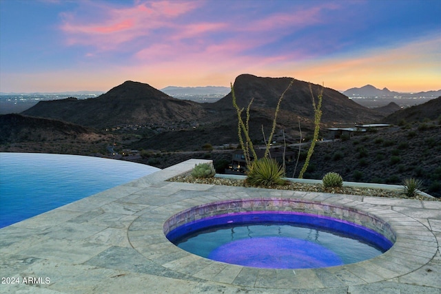 pool at dusk with an in ground hot tub and a mountain view