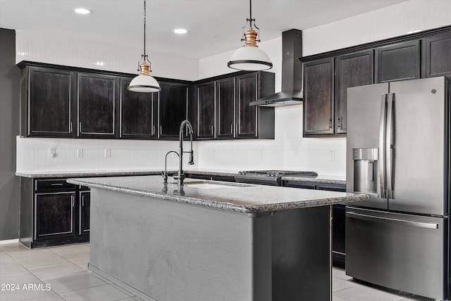 kitchen with stainless steel fridge, sink, wall chimney range hood, hanging light fixtures, and an island with sink