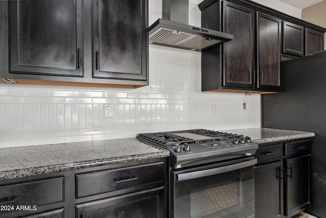 kitchen featuring backsplash, stainless steel gas range oven, black fridge, and wall chimney exhaust hood