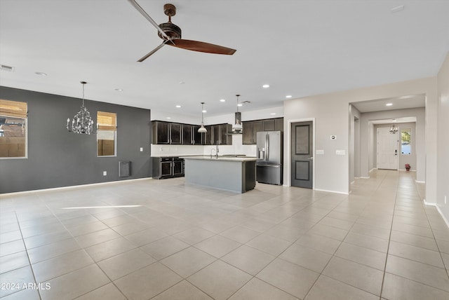 kitchen featuring a center island with sink, decorative light fixtures, stainless steel fridge with ice dispenser, and wall chimney range hood