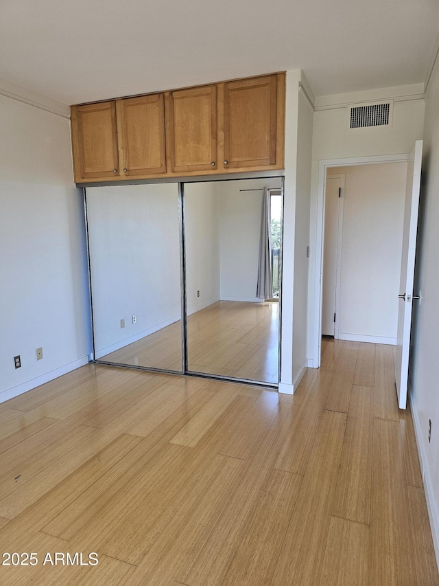 unfurnished bedroom with baseboards, light wood-style flooring, visible vents, and a closet