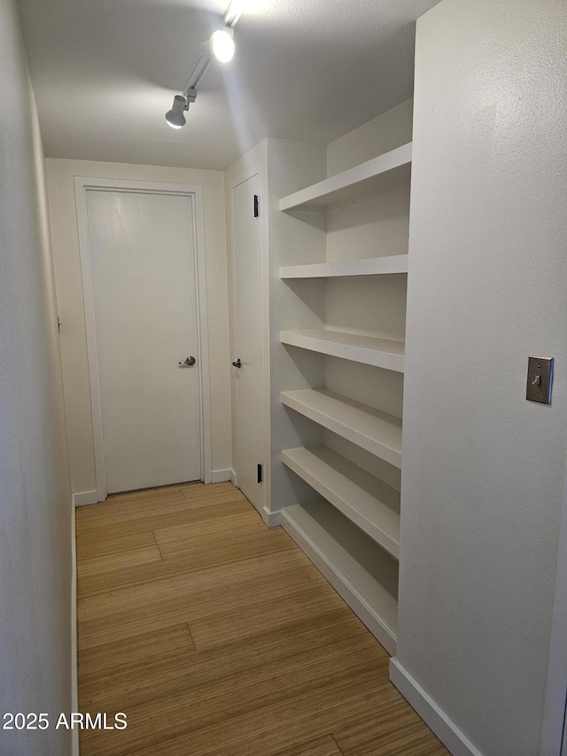 corridor with track lighting, light wood-type flooring, and baseboards