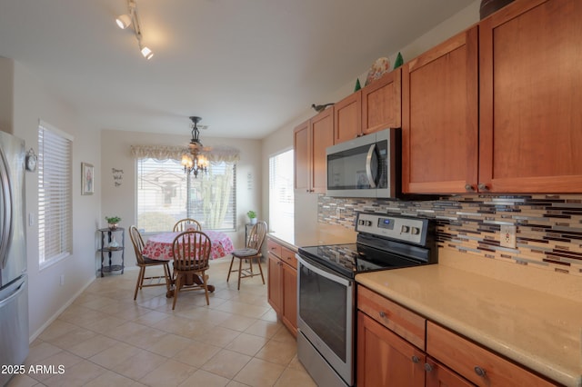 kitchen featuring light tile patterned flooring, an inviting chandelier, decorative light fixtures, appliances with stainless steel finishes, and decorative backsplash