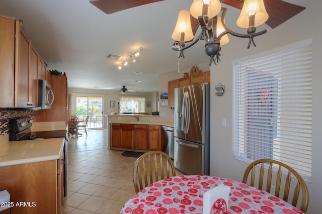 kitchen featuring light tile patterned floors, ceiling fan with notable chandelier, stainless steel appliances, decorative backsplash, and kitchen peninsula