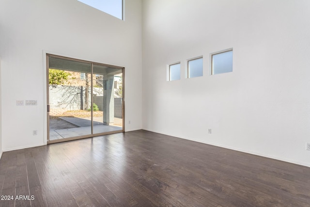 unfurnished room with dark hardwood / wood-style flooring, a towering ceiling, and a healthy amount of sunlight