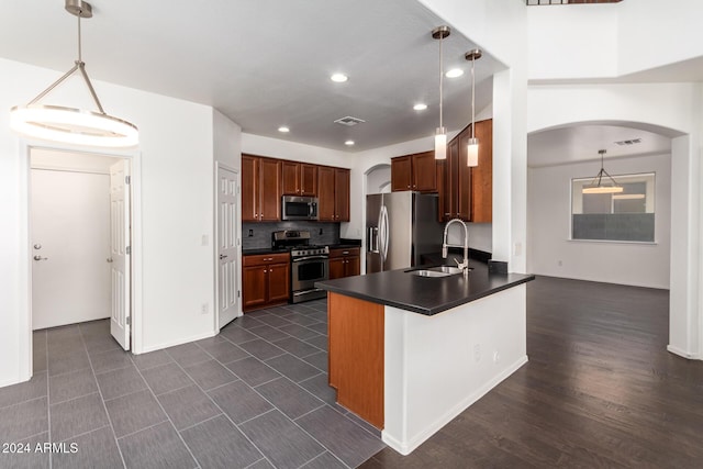 kitchen featuring kitchen peninsula, decorative backsplash, stainless steel appliances, sink, and decorative light fixtures