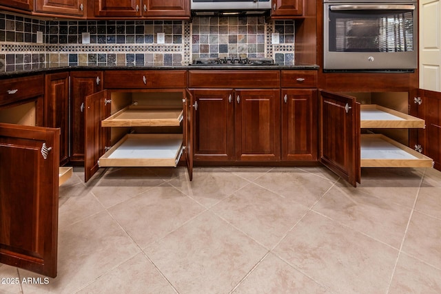 kitchen featuring tasteful backsplash, black gas stovetop, dark stone counters, light tile patterned floors, and oven