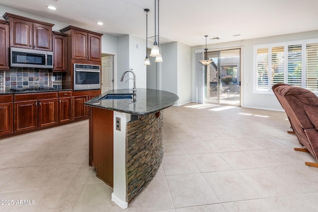 kitchen with appliances with stainless steel finishes, tasteful backsplash, dark stone counters, sink, and pendant lighting