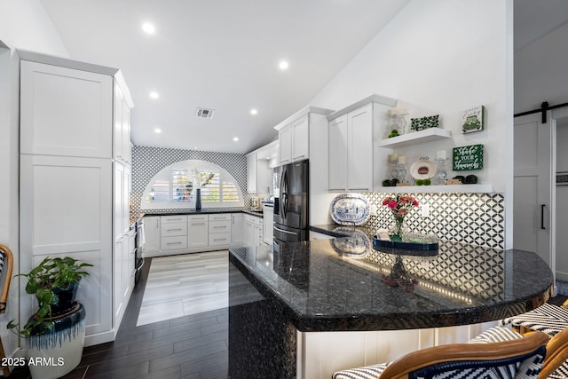 kitchen featuring visible vents, black fridge with ice dispenser, decorative backsplash, a barn door, and a peninsula