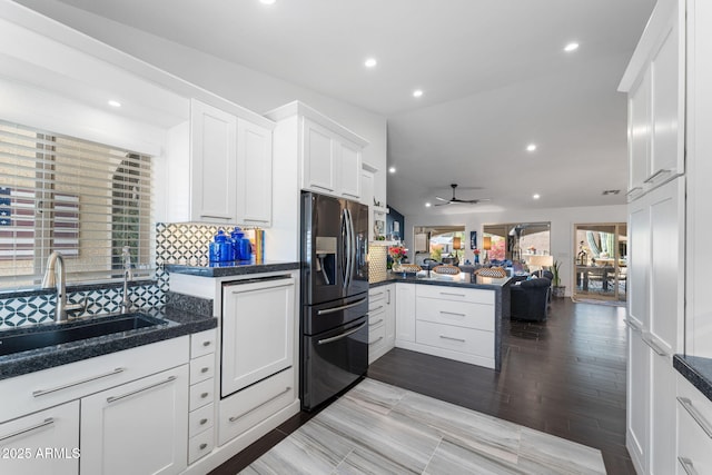 kitchen featuring a peninsula, a sink, refrigerator with ice dispenser, white cabinets, and tasteful backsplash