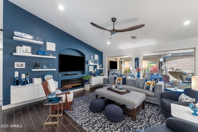 living room with visible vents, wood tiled floor, a glass covered fireplace, vaulted ceiling, and ceiling fan