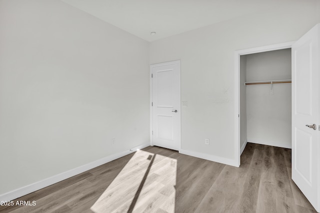 unfurnished bedroom featuring a spacious closet, a closet, baseboards, and wood finished floors