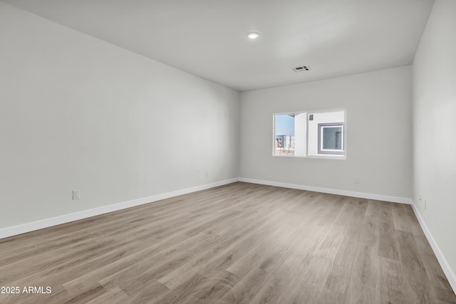 empty room with light wood finished floors, visible vents, and baseboards