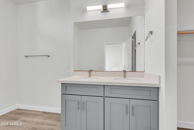 full bathroom with double vanity, a sink, baseboards, and wood finished floors