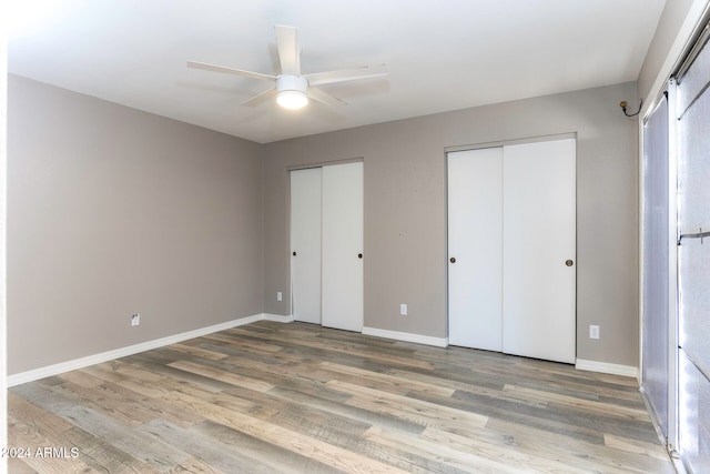 unfurnished bedroom with hardwood / wood-style floors, ceiling fan, and two closets