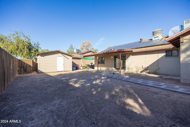 rear view of property with a storage unit, a patio, and solar panels