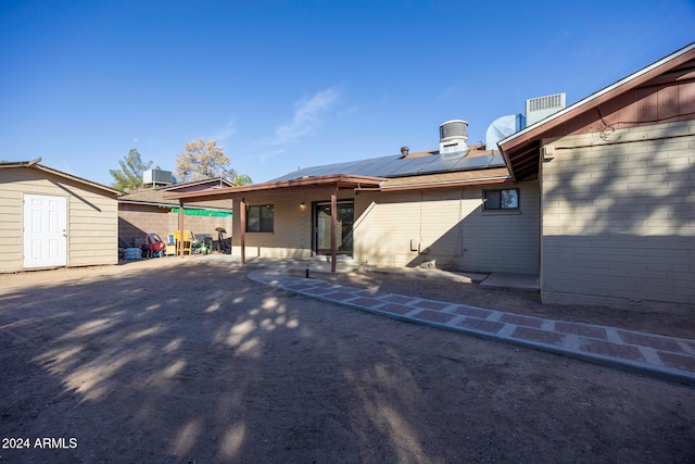 rear view of property featuring solar panels, cooling unit, a patio area, and a storage unit