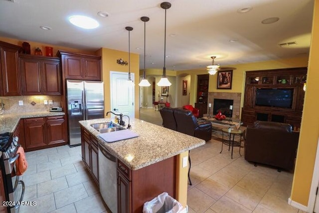 kitchen with backsplash, stainless steel appliances, light tile floors, a tile fireplace, and an island with sink