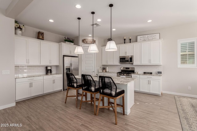 kitchen featuring stainless steel appliances, white cabinetry, light stone counters, and pendant lighting