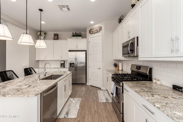 kitchen featuring decorative light fixtures, an island with sink, a breakfast bar, white cabinetry, and appliances with stainless steel finishes