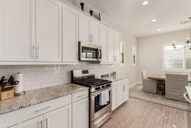 kitchen with light stone counters, appliances with stainless steel finishes, hanging light fixtures, and white cabinetry