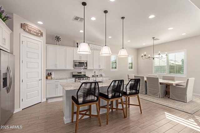 kitchen with a center island with sink, appliances with stainless steel finishes, a notable chandelier, pendant lighting, and white cabinets