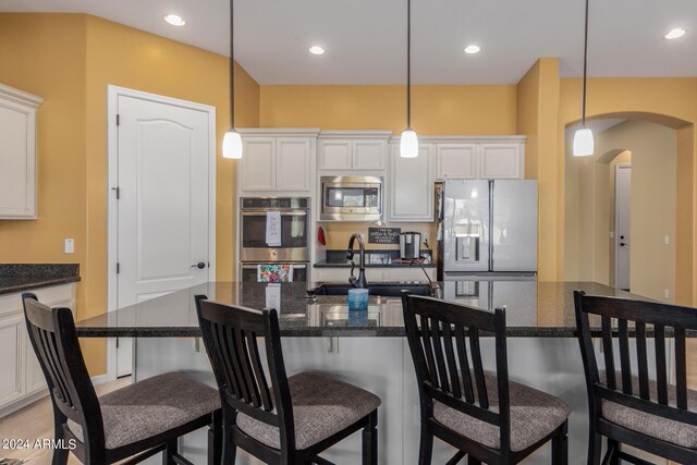 kitchen with appliances with stainless steel finishes, hanging light fixtures, a kitchen island with sink, and white cabinets