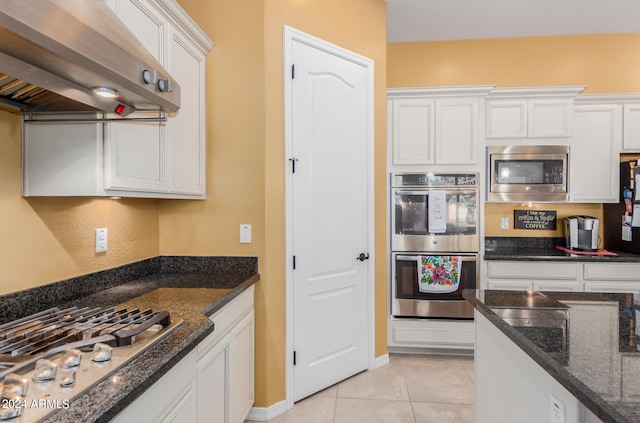 kitchen featuring white cabinets, light tile patterned floors, appliances with stainless steel finishes, range hood, and dark stone countertops