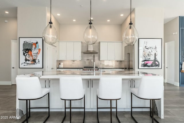 kitchen featuring pendant lighting, tasteful backsplash, white cabinets, a large island, and wall chimney range hood