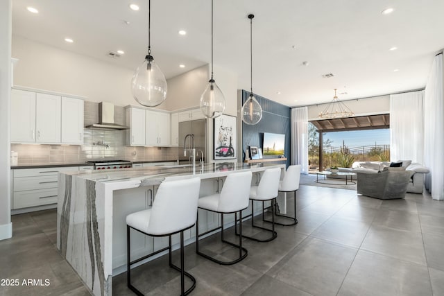 kitchen featuring a spacious island, wall chimney exhaust hood, a kitchen bar, pendant lighting, and white cabinets