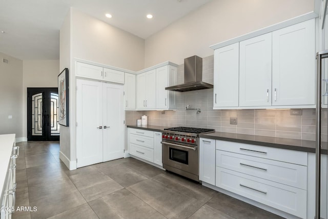 kitchen featuring backsplash, white cabinets, luxury stove, and wall chimney range hood