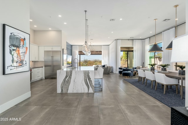 kitchen with hanging light fixtures, plenty of natural light, built in fridge, and white cabinets