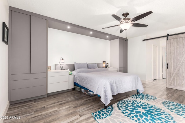 bedroom with recessed lighting, baseboards, a barn door, and light wood-style floors