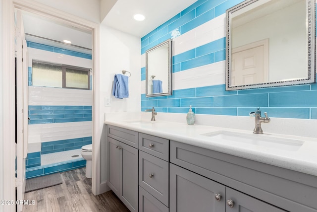 bathroom with double vanity, a sink, a tile shower, and toilet