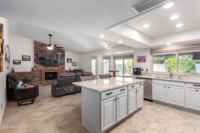 kitchen featuring a fireplace, ceiling fan, a center island, a sink, and dishwasher