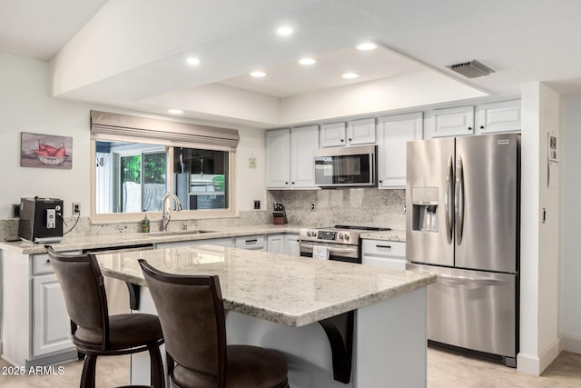 kitchen featuring a sink, light stone counters, stainless steel appliances, and visible vents