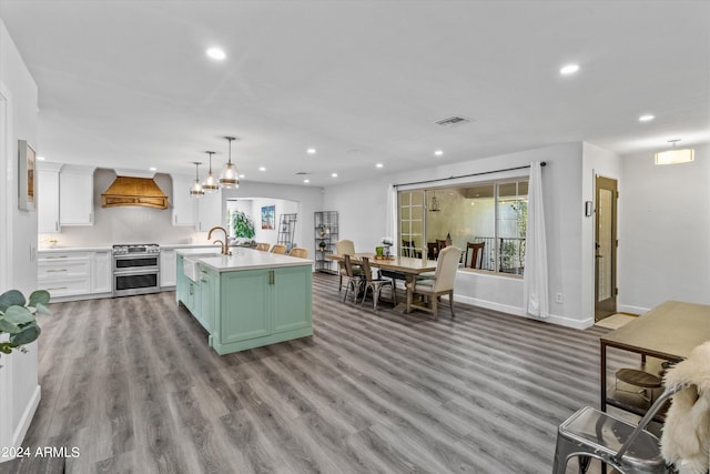 kitchen with a kitchen island with sink, white cabinets, light hardwood / wood-style flooring, double oven range, and premium range hood