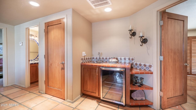 bar with light tile patterned floors, sink, tile countertops, and wine cooler