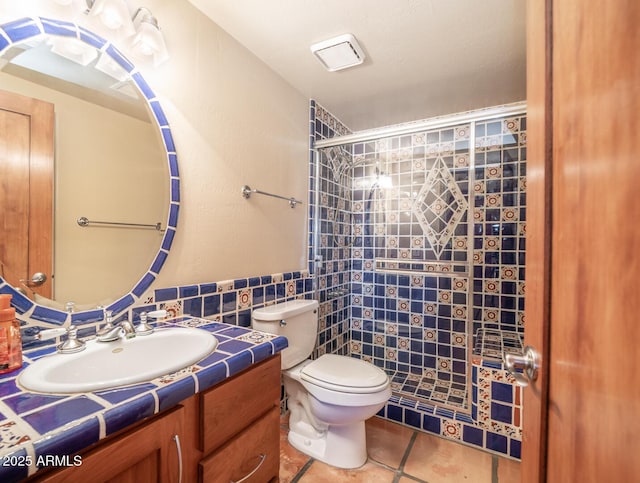 bathroom featuring vanity, toilet, tiled shower, and tile patterned flooring