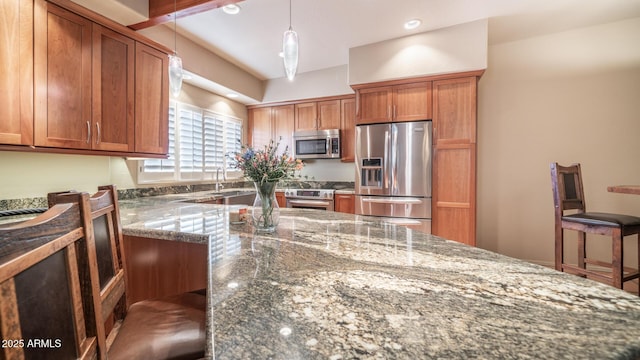 kitchen with stainless steel appliances, dark stone countertops, hanging light fixtures, and a breakfast bar