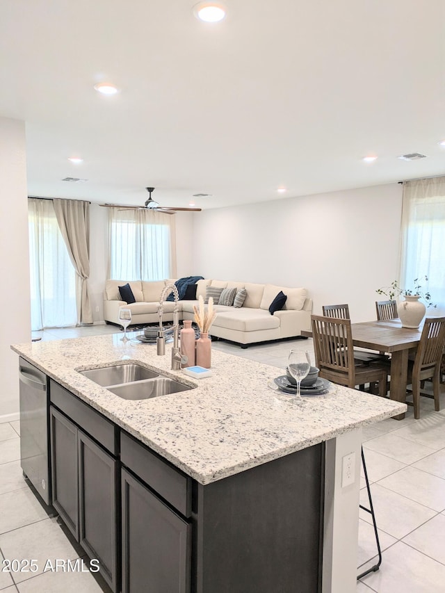 kitchen with an island with sink, light stone countertops, stainless steel dishwasher, and light tile patterned flooring