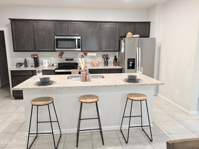 kitchen featuring sink, a breakfast bar area, a kitchen island with sink, light stone counters, and stainless steel appliances