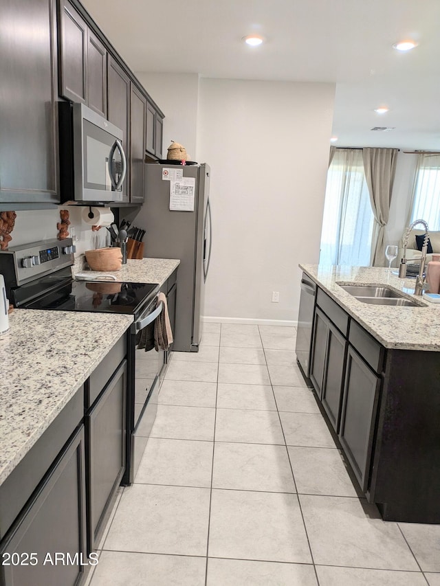 kitchen featuring sink, dark brown cabinets, light tile patterned floors, stainless steel appliances, and light stone countertops