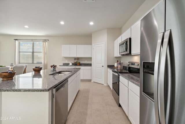 kitchen with a kitchen island with sink, dark stone counters, white cabinets, sink, and stainless steel appliances