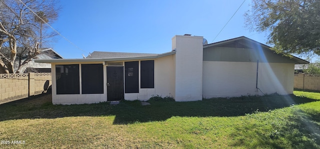 rear view of house featuring a yard, a fenced backyard, a chimney, and a sunroom