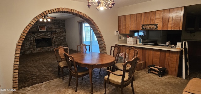 dining room featuring carpet, a fireplace, arched walkways, and a chandelier