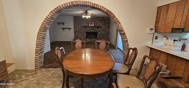 dining room featuring arched walkways, light colored carpet, a fireplace, and ceiling fan